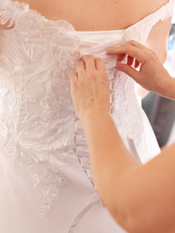 détailles de la mariée qui enfile sa robe avec l'aide de sa témoin