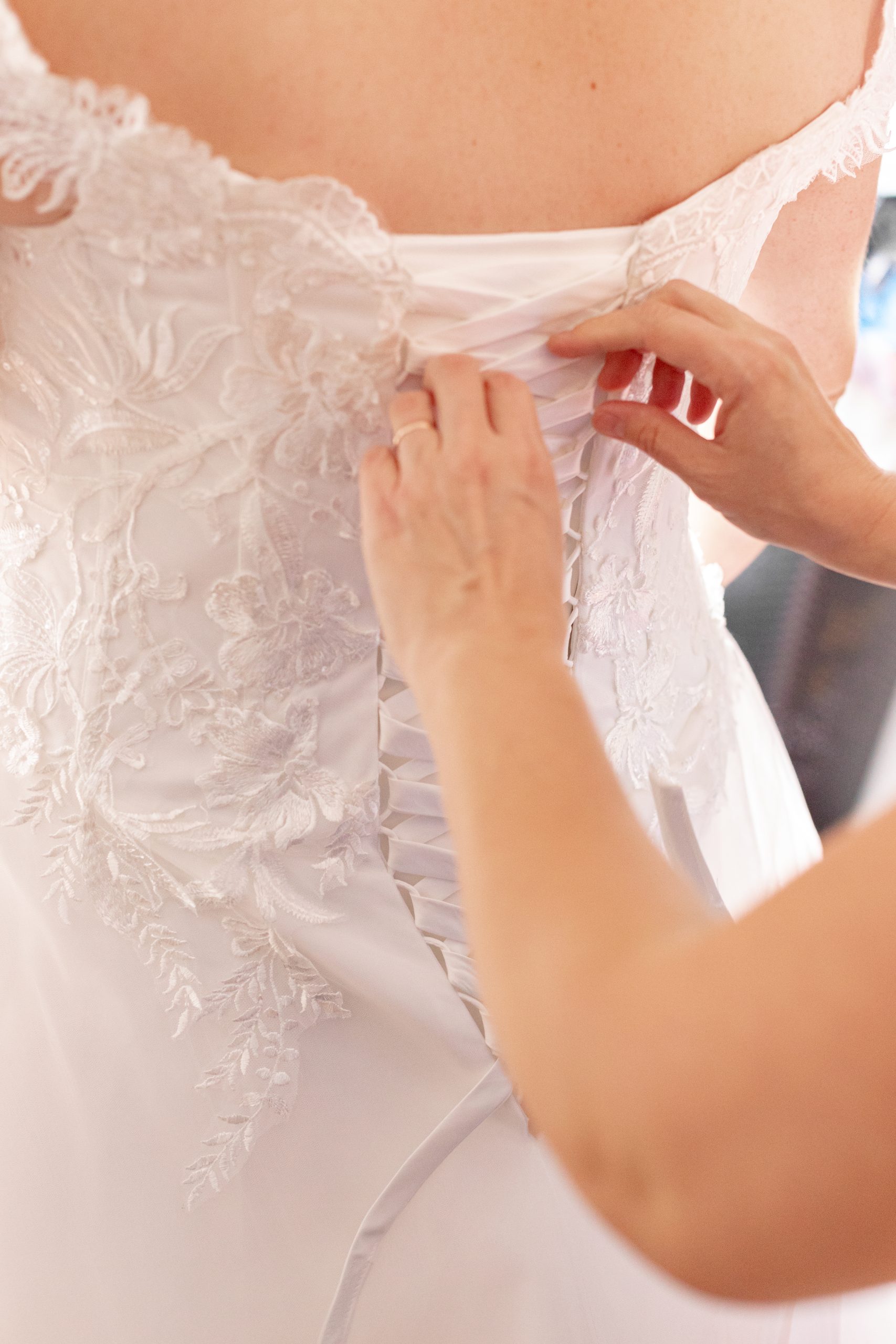 détailles de la mariée qui enfile sa robe avec l&#039;aide de sa témoin